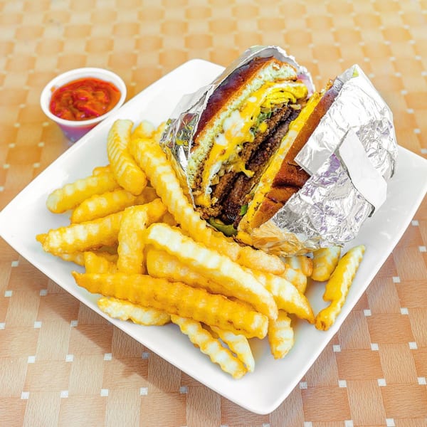 A large cheeseburger wrapped in foil, cut in half, with crinkle-cut fries and a side of salsa.
