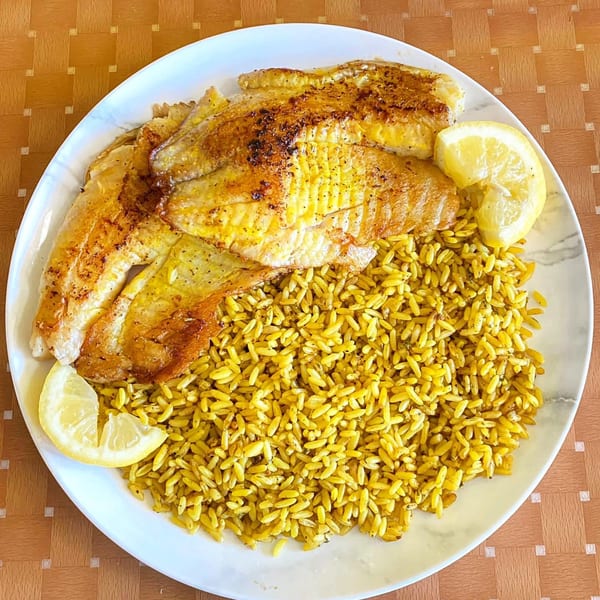Golden-brown fish fillets with lemon wedges and yellow rice on a white plate.