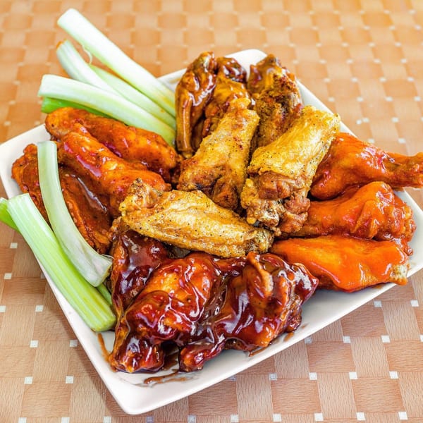 A white platter filled with various Lokman's Best Wings, including BBQ, buffalo, and lemon pepper, with celery sticks.
