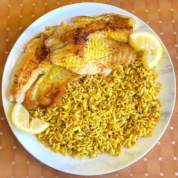 Seasoned fish fillets and yellow rice with lemon wedges on a white plate.