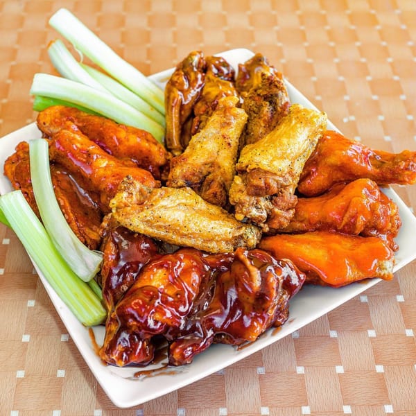 A platter of Lokman's Best Wings with various sauces and celery sticks.